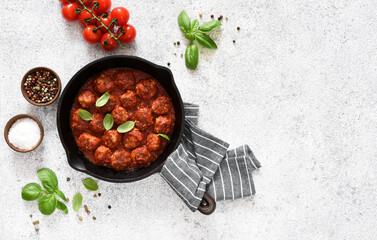 Meat balls with tomato sauce in a frying pan on a light concrete background.