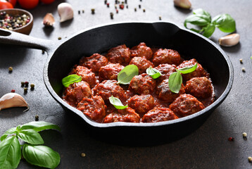 Meat balls with tomato sauce with garlic and basil in a frying pan on a brown background.