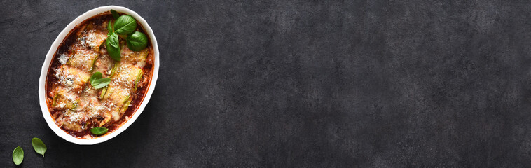 Baked zucchini rolls with ricotta cheese and tomato sauce and parmesan on a black background.