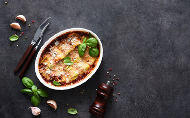 Baked zucchini rolls with ricotta cheese and tomato sauce and parmesan on a black background.