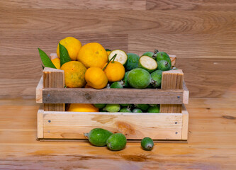 Assortment of fruits in wooden box, on wooden background. The concept of healthy food. Fresh Ripe feijoa (lat. Acca sellowiana) and mandarin