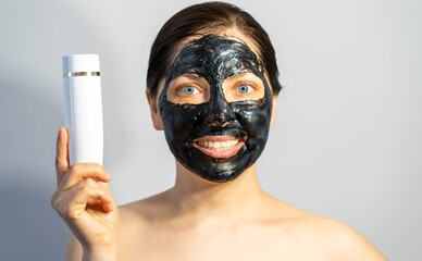 Emotional Woman with black charcoal face mask and white tube of cream in her hands