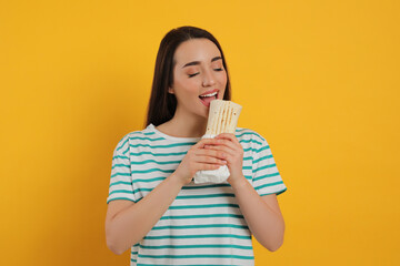 Young woman eating tasty shawarma on yellow background