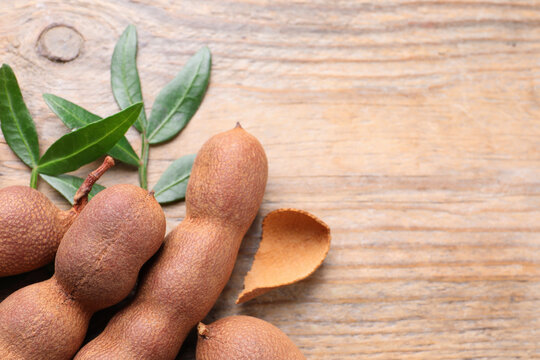 Ripe tamarinds and fresh leaves on wooden table, flat lay. Space for text