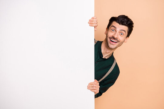 Photo of funny guy hold white wall empty space wear green shirt suspenders isolated beige background