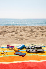 Towel, sunscreen, flip-flops, sunglasses and smart phone on the beach. Summer concept.