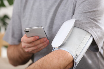 Man checking blood pressure with modern monitor and smartphone indoors, closeup