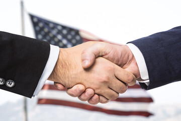 Fototapeta na wymiar Two businessmen shake hands on the background of USA flag, partnership concept, close up