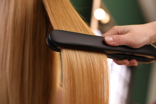 Stylist straightening woman's hair with flat iron in salon, closeup