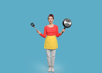 Housewife with frying pan and spatula on light blue background