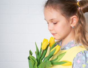 Beautiful young girl in a yellow blouse with tulips flowers in her hands on a light background