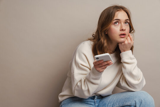 Young puzzled woman using mobile phone while sitting