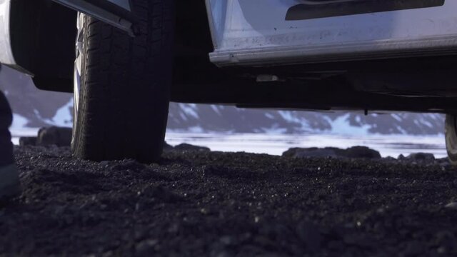 Closeup of adventurers boots landing on black sand as he jumps out of a van.