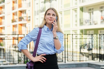 Young businesswoman talking on smartphone, street office building background