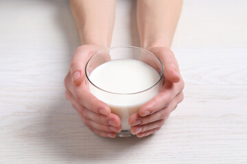 Woman holding glass of milk at white wooden table, closeup