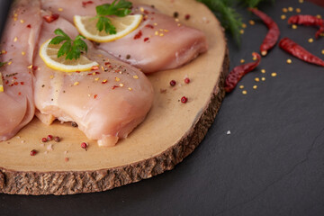 raw chicken fillet with garlic, pepper and rosemary on wooden on chopping board. fresh fillet. fresh chicken meat, chicken fillet with spices at black stone table. top view with copy space..