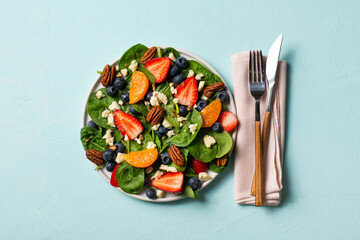 Summer salad with berries, cheese and spinach on blue background