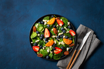 Summer salad with berries, cheese and spinach on blue background