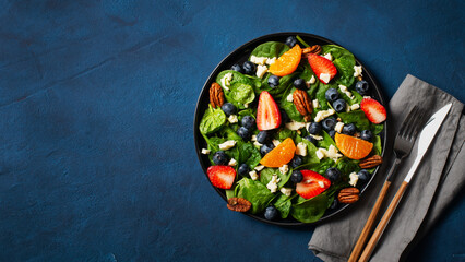 Summer salad with berries, cheese and spinach on blue background