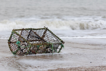 Lobster creel washed up on the beach. Crab pot fishing basket. - obrazy, fototapety, plakaty