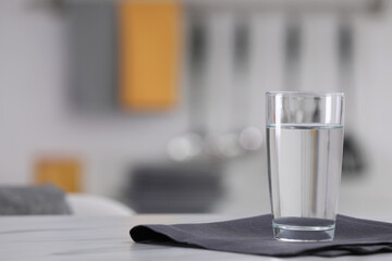 Glass of water and napkin on white table against blurred background. Space for text