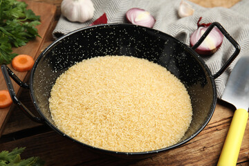 Uncooked rice in wok on wooden table, closeup