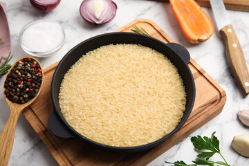 Uncooked rice in wok and products on white marble table