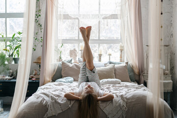 Young woman raised legs up, lying in bed © brizmaker