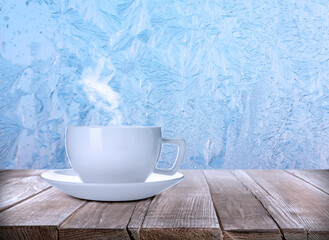 Cup of hot tea on table near window covered with frost