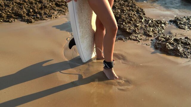 Piernas de una chica en la arena con tabla de surf