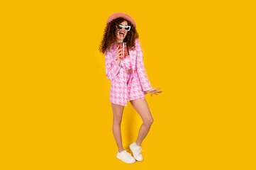 Girl in summer outfit wearing pink color and enjoying while drinking a red cocktail. Posing on the yellow background.