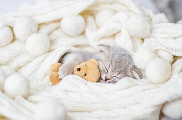 A small purple kitten is lying on a white knitted background and sleeping. Postcard for the holiday concept.