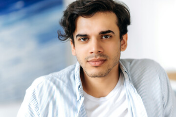 Close up portrait of a charismatic handsome confident mixed race hispanic guy, wearing blue shirt, looking directly at the camera with friendly smile