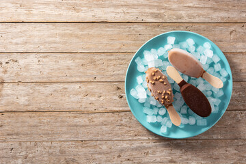 Chocolate popsicles and crushed ice on blue plate on wooden table.Top view. Copy space