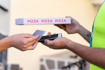 Woman paying bill through smartphone using NFC technology at a delivery man. Satisfied customer paying through mobile phone using contactless technology. Focus on hand.
