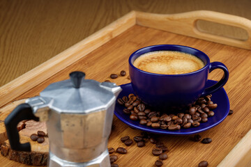 Cup of coffee and coffee beans on a platter and geyser coffee maker on a wooden tray