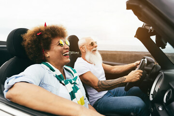 Senior trendy couple inside a convertible car on holiday time - Travel, fashion and joyful elderly...