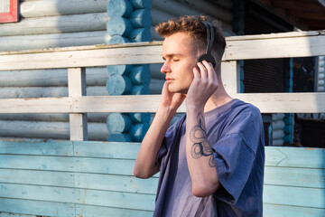 teenager in headphones with a snake tattoo on his arm listening to music with closed eyes in the park