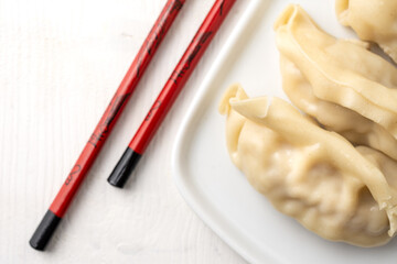 Aerial view of white plate with gyozas and red and black chopsticks, on white background, horizontal, with copy space