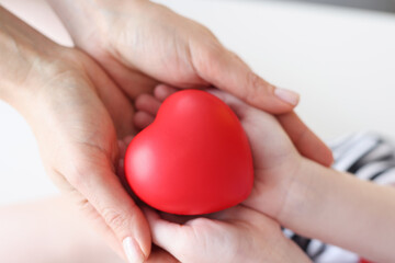 Little girl and mother hands holding red toy heart closeup