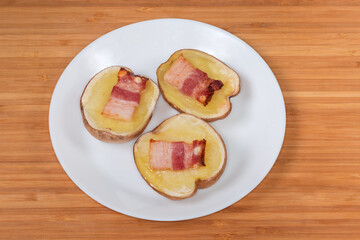 Potato halves baked with bacon slices on white dish