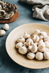 Fresh mushrooms champignons in wooden plate on the kitchen table.