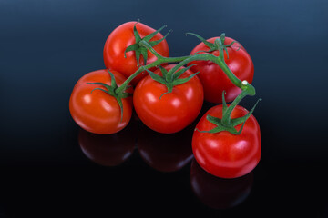 Red tomatoes on branch on a dark surface