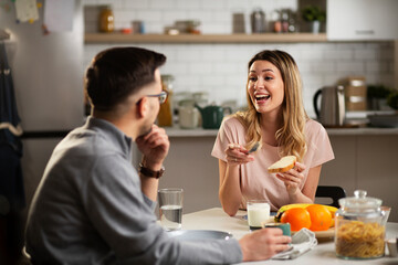 Beautiful young woman enjoying in breakfast with boyfriend. Happy young couple drinking coffee and eating sandwich at home..