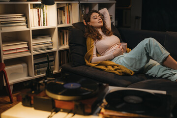 Fototapeta na wymiar woman relaxing on sofa at her home and listening to a music on record player
