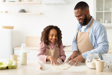 Cheerful afro man and his child daughter kneading dough