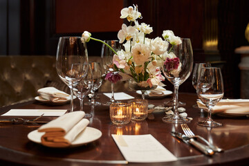 beautifully set table in a restaurant for several people with transparent glasses and a floral arrangement of white orchids and other white flowers in the center