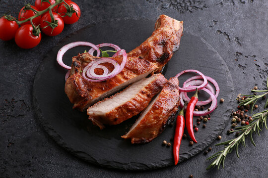 Meat and barbecue. Roast pork ham on a black board with onions, spices, pepper, rosemary and vegetables on a black table. Background image, copy space