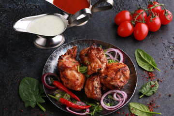 Fried chicken pieces with fresh herbs, coriander, vegetables, onions, spices and sauces on a black plate. Background image, copy space