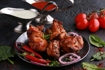 Fried chicken pieces with fresh herbs, coriander, vegetables, onions, spices and sauces on a black plate. Background image, copy space